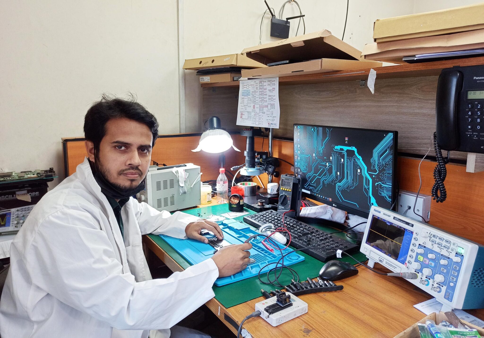 SafeTech trainer repairing a laptop motherboard under a microscope